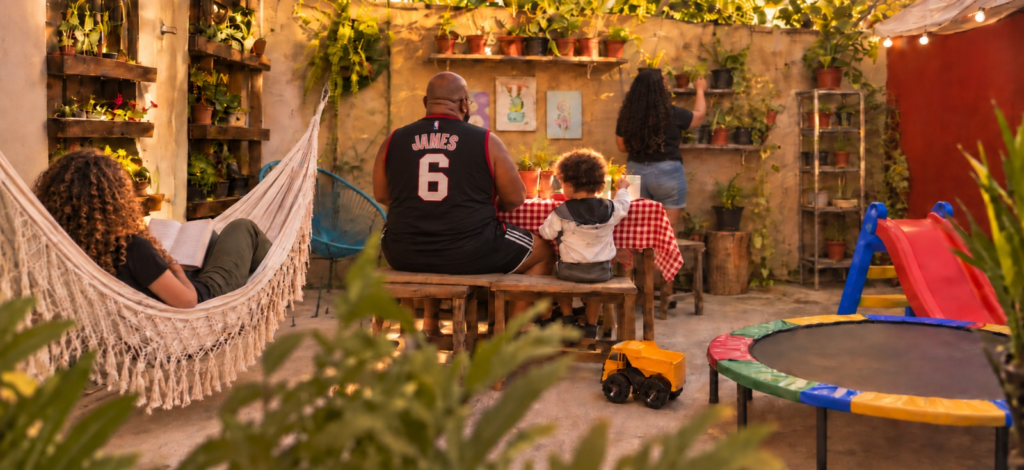 Família reunida no quintal de casa, criança brincando entre brinquedos e plantas